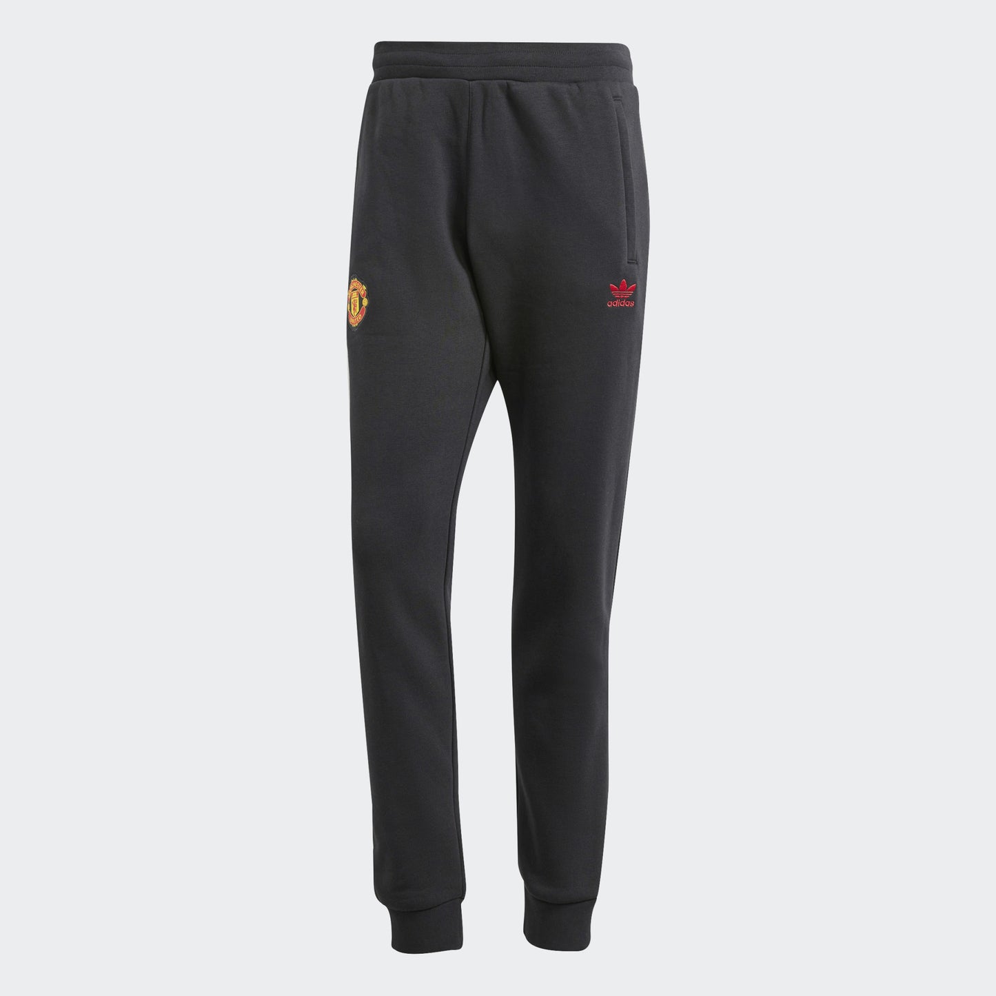 A pair of black Adidas Manchester United Essentials Trefoil Track Pants with the club's logo on the left leg.